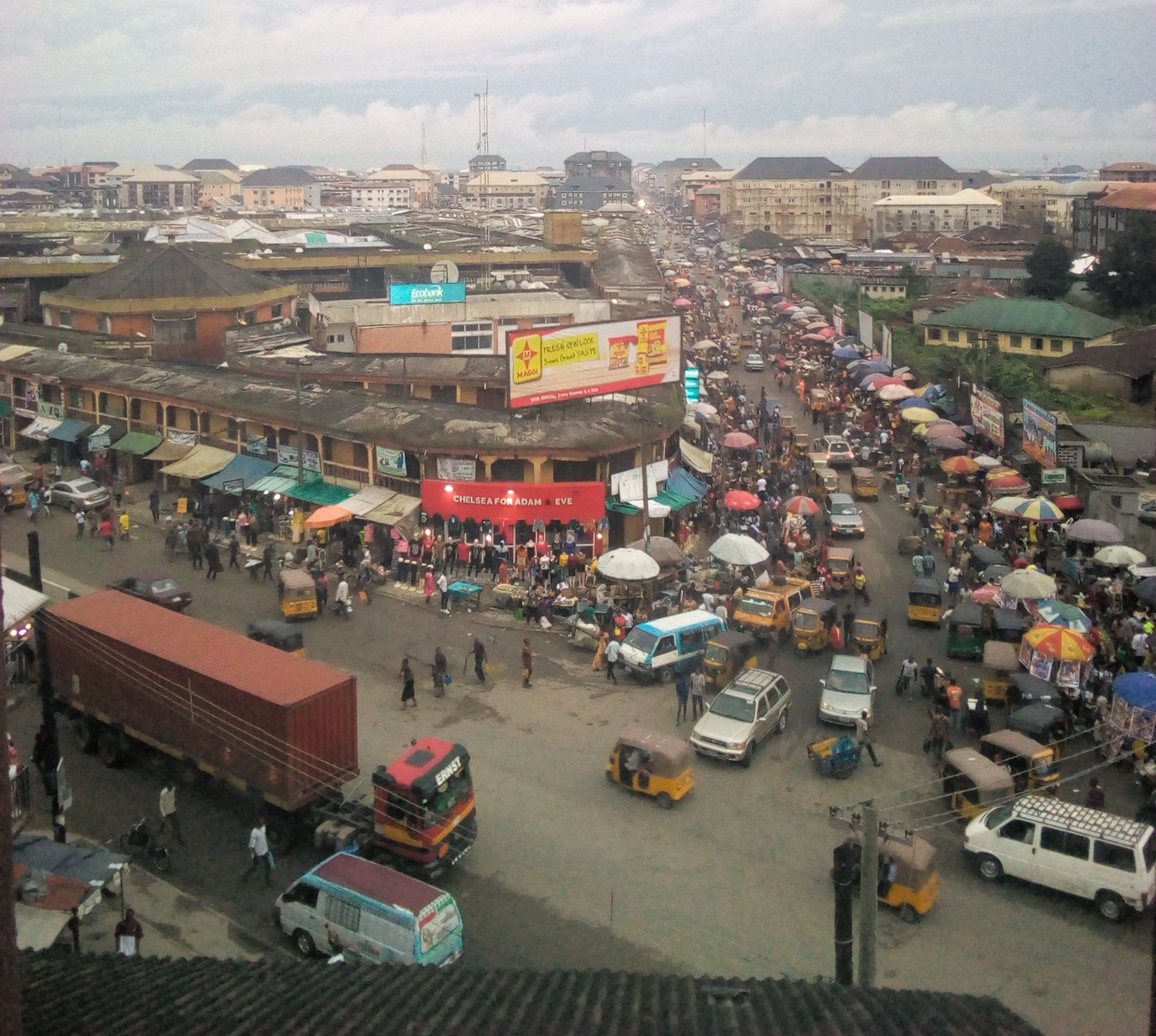  A densely populated market with a lot of shops, predominantly having two floors, a lot of vehicles, buses, tricycles, heavy trucks carrying goods and humans without number in the Ariaria international market of Aba